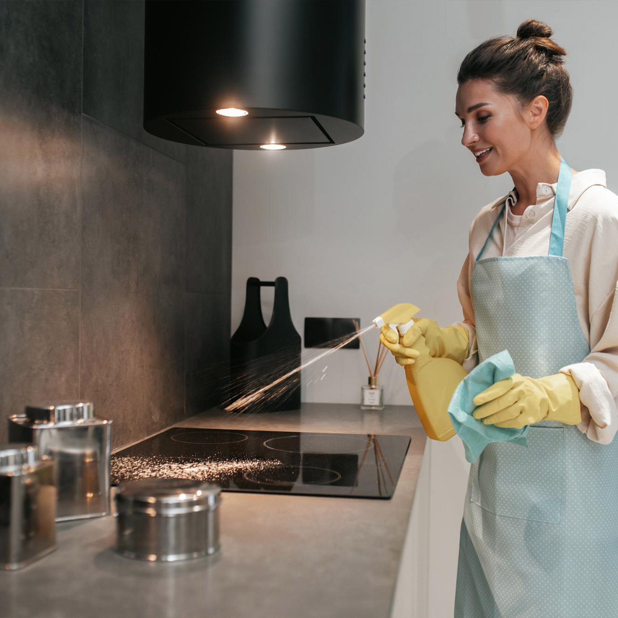 Woman cleaning a stovetop with a spray and cloth.